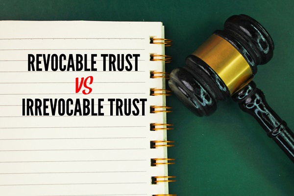 Open notebook with the words "Revocable Trust vs Irrevocable Trust" next to a judge’s gavel on a green surface.