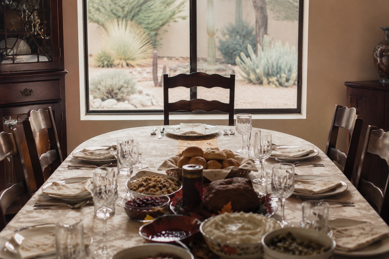 An empty wooden chair sits at the head of a fully set dining table with a holiday feast, looking out a window at an Arizona desert landscape, symbolizing an empty seat from a deceased beneficiary in an Arizona estate plan.
